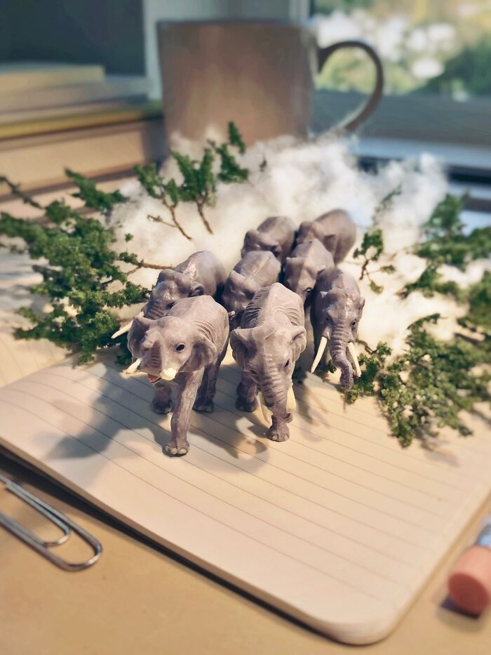 Artist Derrick Lin turns his office desk into intricate diorama sets, showcasing miniature elephants amidst trees and clouds.