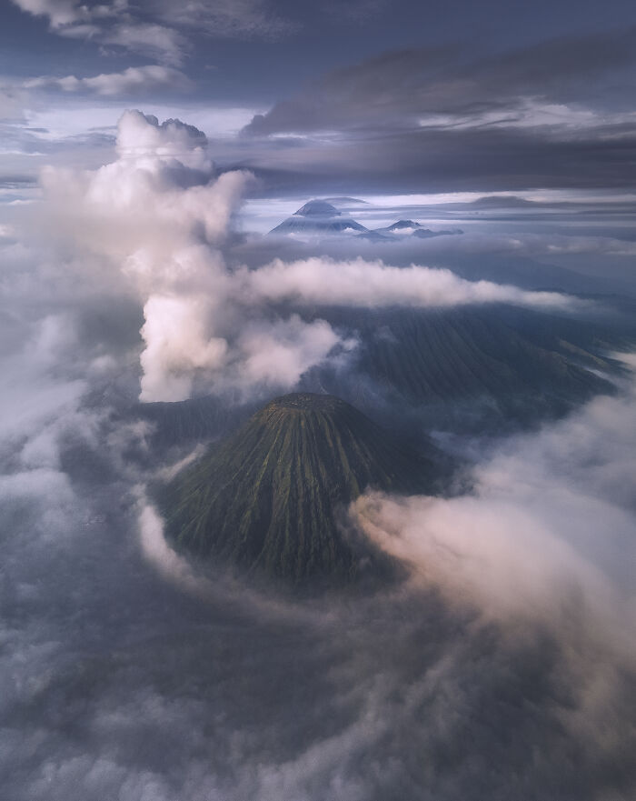 An aerial photograph of a volcanic mountain emerging from a sea of clouds, awarded at the 2026 competition.