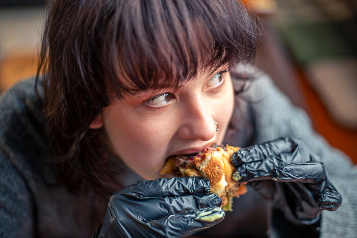 Woman in black gloves taking a large bite of a sandwich; strange reasons people got fired.
