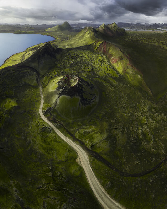 Spectacular aerial photograph of a moss-covered volcanic crater with a winding road and distant lake.
