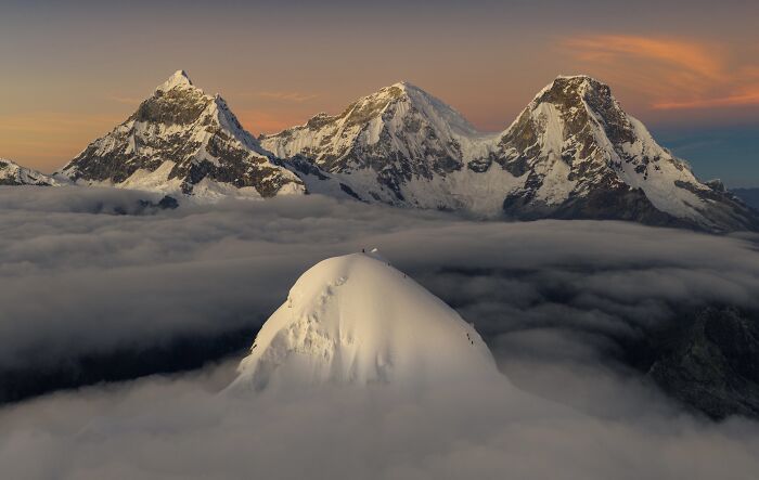 Spectacular aerial photograph of snow-capped mountains peaking through clouds, awarded at the Aerial Photographer of the Year competition.