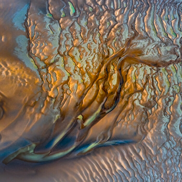 An aerial photographer award-winning capture of colorful, fluid abstract patterns in shades of orange, blue, and green, resembling textured earth.