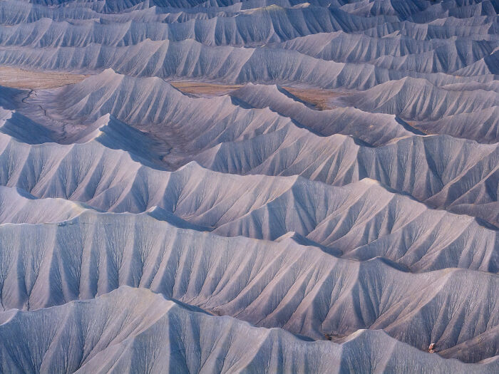 A spectacular aerial photograph displaying an endless expanse of ridged, wave-like grey hills and valleys, a top aerial photographer award.