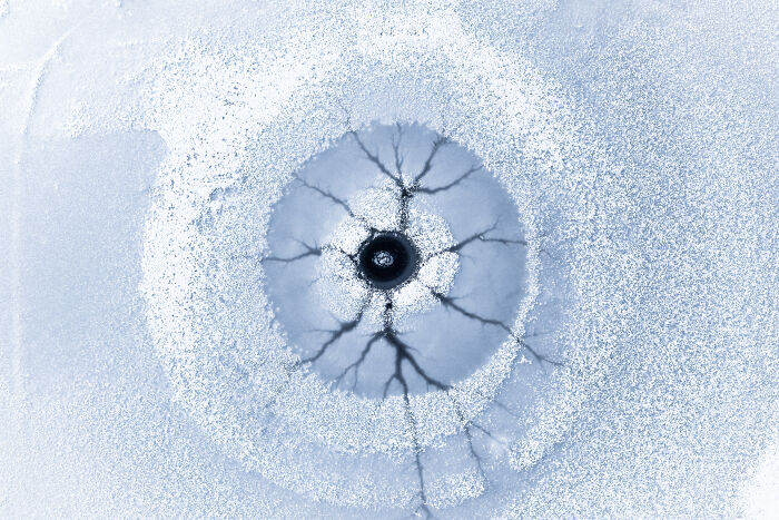 A stunning aerial photographer award-winning shot of a frozen lake with a dark hole and ice cracks, captured from above.