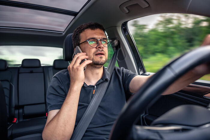 A man driving a car while talking on the phone, illustrating a potentially bad pocket dial story.