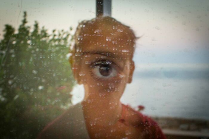 A child's face with a magnified eye visible through a rain-streaked window, a serendipitous moment captured by a street photographer.