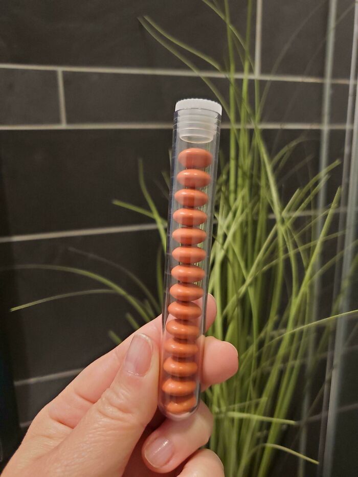 A hand holding a test tube filled with orange pills, showing the consumerism and price difference.