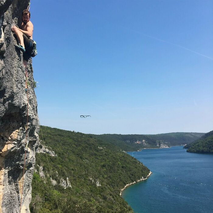 A man rock climbing on a cliff face, glasses floating in the air, a moment before disaster struck.