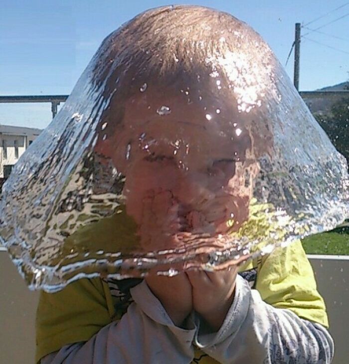 A child with a perfect dome of water on their head, a hilarious photo taken moments before the water falls.