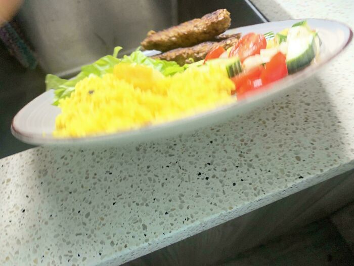 A plate of food, including yellow rice, meat, and a salad, sliding off a counter in a photo before disaster.