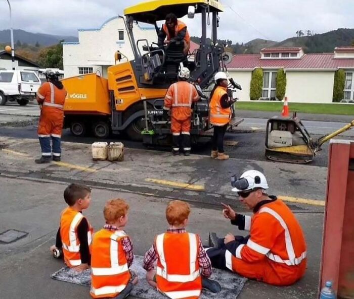 Construction workers in orange vests and hard hats explain their work to three young boys, a soul-healing interaction.