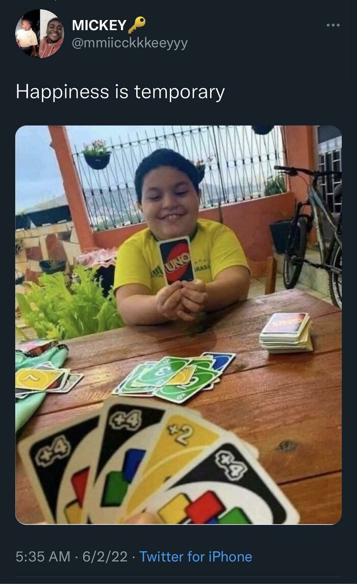 A young boy smiles holding an UNO card, unaware of the +4 and +2 cards in the foreground, moments before disaster.