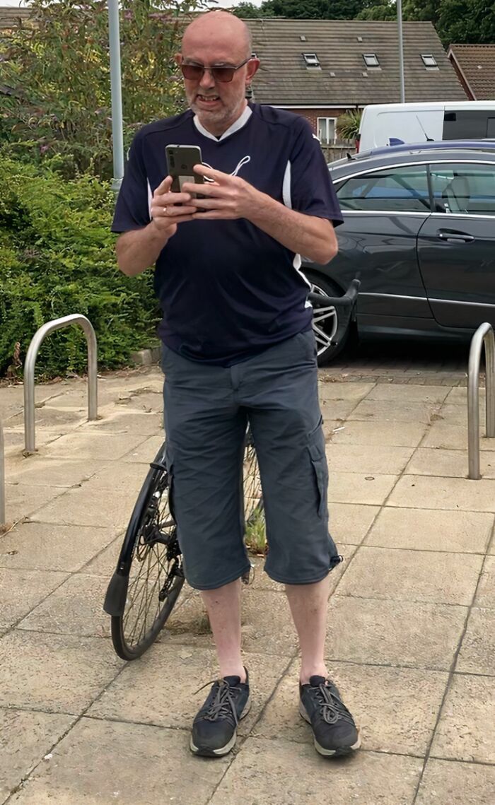 A man with sunglasses looking at his phone, standing next to a bicycle. Stories of entitled men ignoring boundaries.