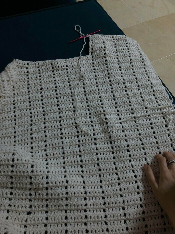 A close-up of a beautiful, incomplete white crochet garment, showcasing the intricate stitches by an enthusiast.