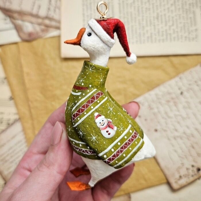 Handmade cotton wool creation of a duck wearing a green Christmas sweater and Santa hat, held in a hand.