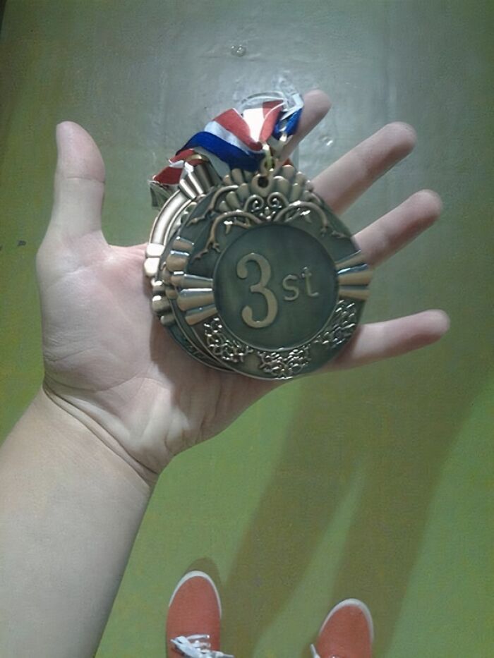 A hand holding a bronze medal that incorrectly reads '3st', showcasing a 'You Had One Job' fail.