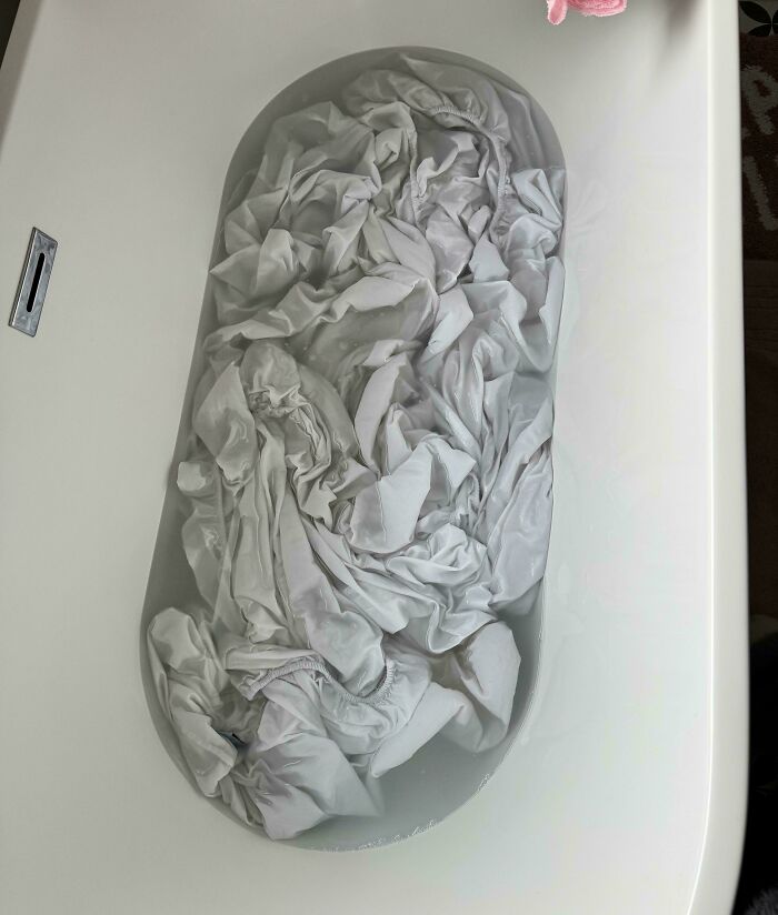 An optical illusion of a bathtub filled with water and white laundry, looking like a giant ear.