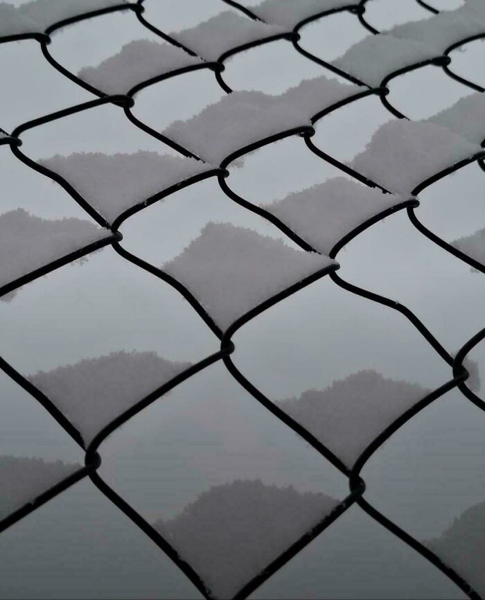 An optical illusion of snow on a chain-link fence resembling mountain peaks.