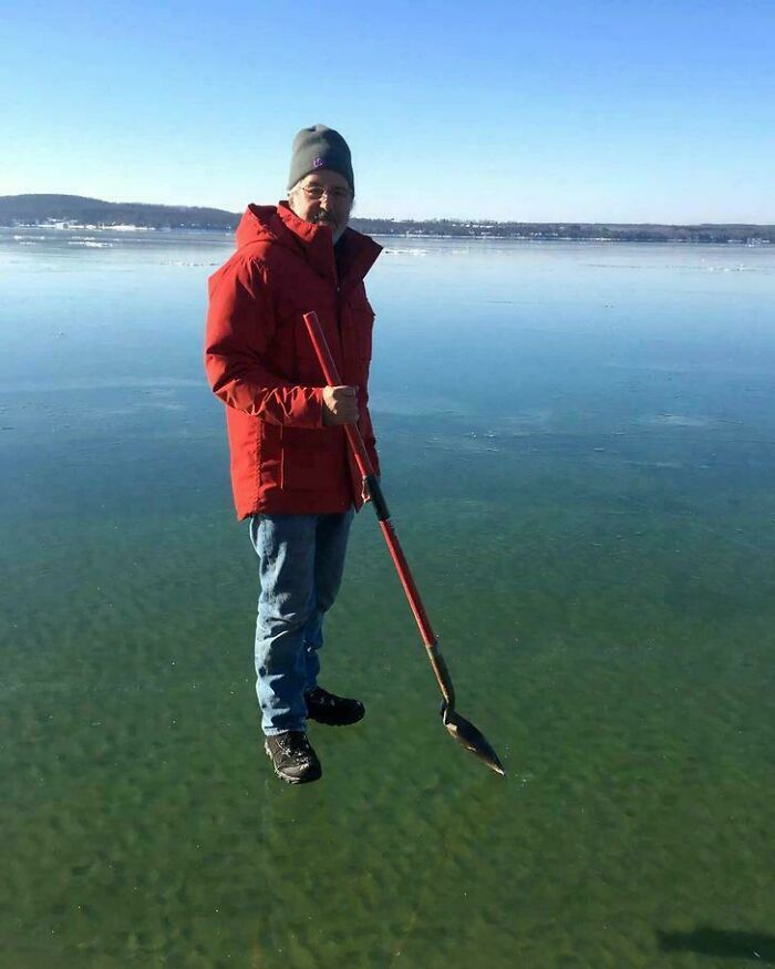 A man appearing to float above a frozen lake while holding a shovel, a real life optical illusion.