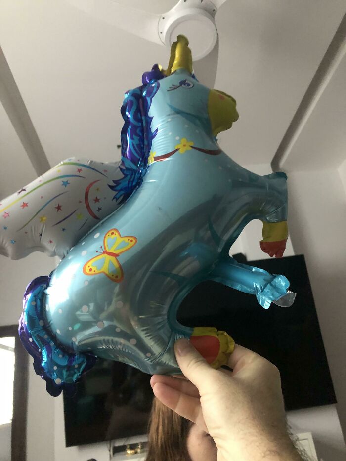 A unicorn balloon with misplaced wings, held by a hand, an example of designer failure.