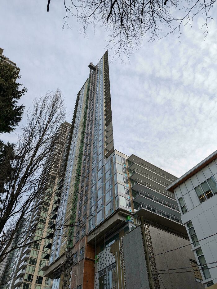 A tall, thin building with a triangular roofline, creating a striking optical illusion against the cloudy sky.