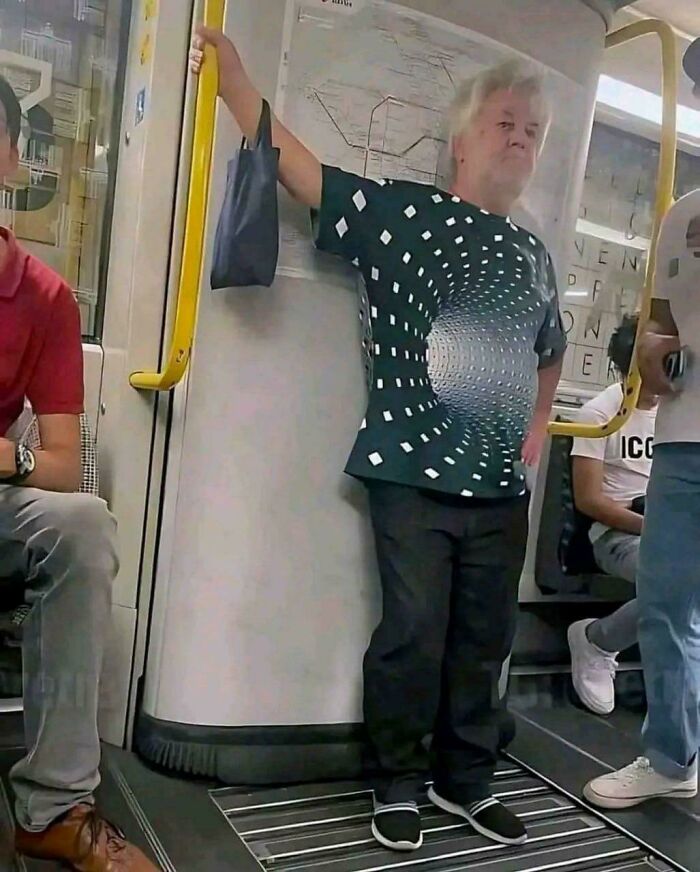 A man on a train wearing a black shirt with a white optical illusion design, resembling a tunnel.