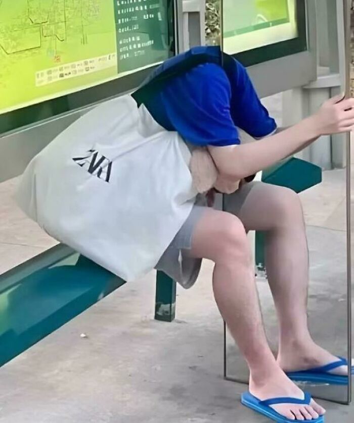 A person at a bus stop with a white ZARA bag over their head, reflecting in a mirror, creating a confusing optical illusion.