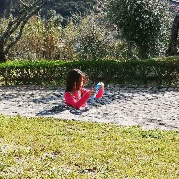 A young girl appears to be partially submerged in a paved pathway, creating a visual optical illusion in a park setting.