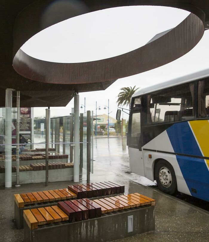 A bus stop with a circular roof, where the bus is positioned in a way that suggests a designer's oversight.