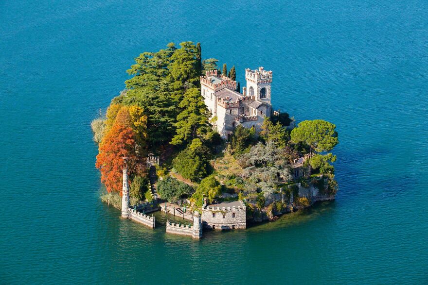 An interesting and beautiful castle on a small island surrounded by clear blue water and vibrant trees.