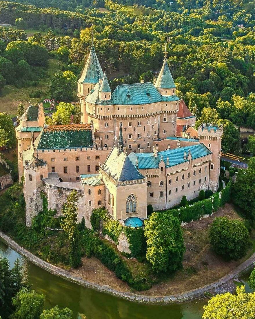 Aerial view of a beautiful historic castle surrounded by lush green forests and a winding river.