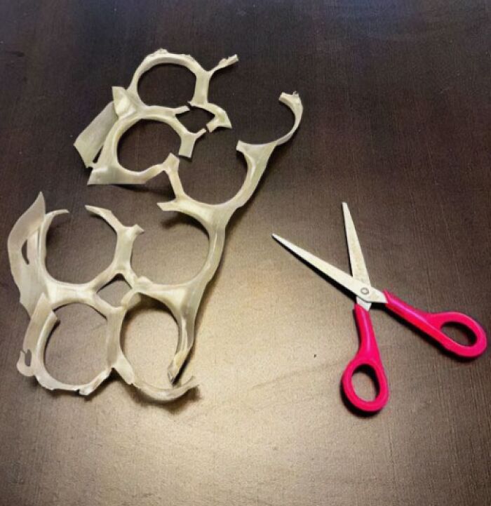 A pair of pink scissors next to cut-up plastic can rings, a 90s kids meme.