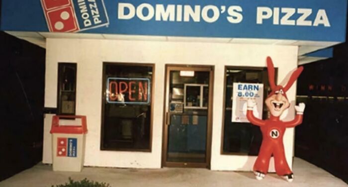 A Domino's Pizza storefront with a red Noid mascot, a throwback meme for 90s kids.