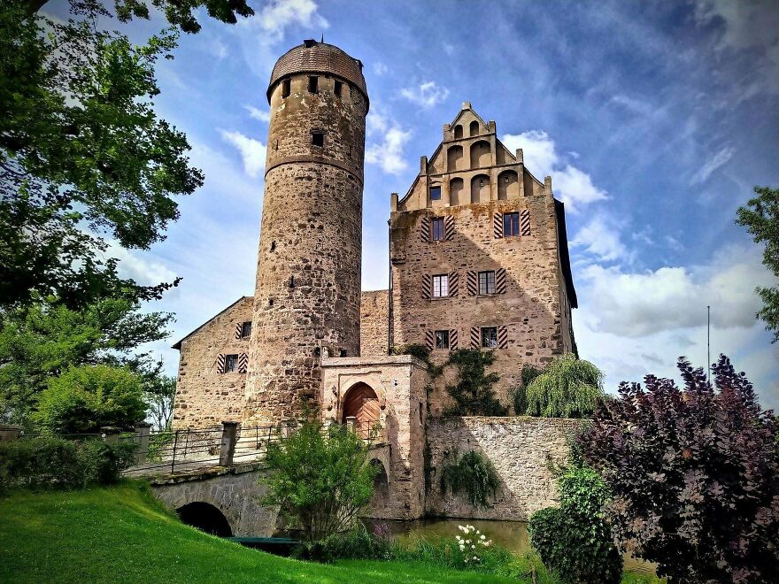 Beautiful castle with a tall round tower, surrounded by lush green trees and a moat, making an interesting photo.