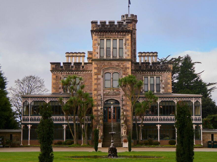 Beautiful stone castle with a fountain in front and manicured lawns, offering interesting architecture.
