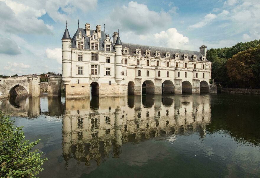 Beautiful white castles spanning across a river with arches, reflecting perfectly in the water under a cloudy sky.