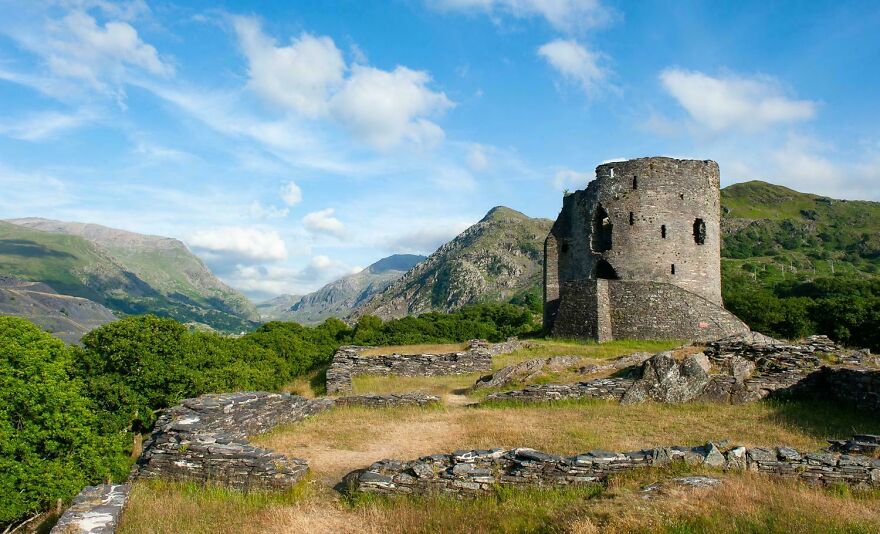 Interesting ancient castles ruin with mountains and blue sky in the background, surrounded by dry grass and rocks.