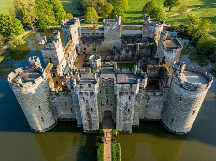 Aerial view of a beautiful and interesting medieval castle with a moat, surrounded by green trees.