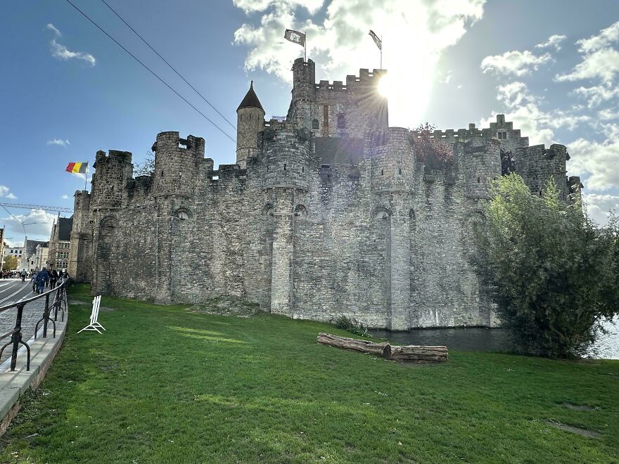 Interesting and beautiful medieval castle with stone walls and flags, illuminated by the sun, next to a river.