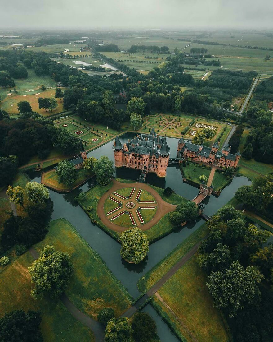 Aerial view of a beautiful and interesting castle surrounded by a moat and lush green gardens.