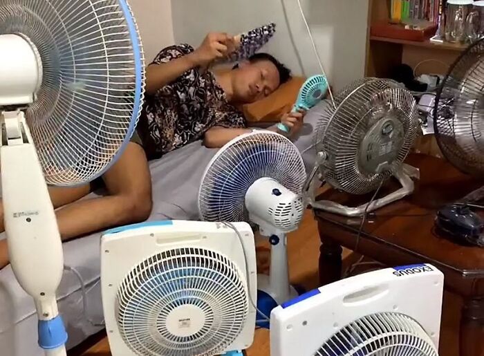 A man surrounded by many fans, trying to escape the summer heat. A funny meme about summer heat.