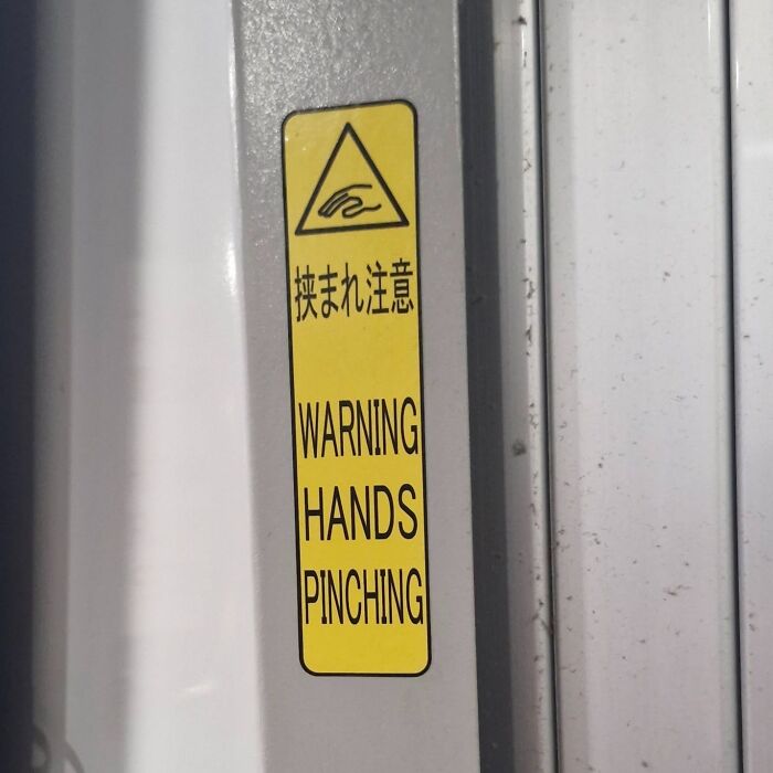 A yellow warning sticker in Japan that says WARNING HANDS PINCHING, a hilarious example of getting lost in translation.