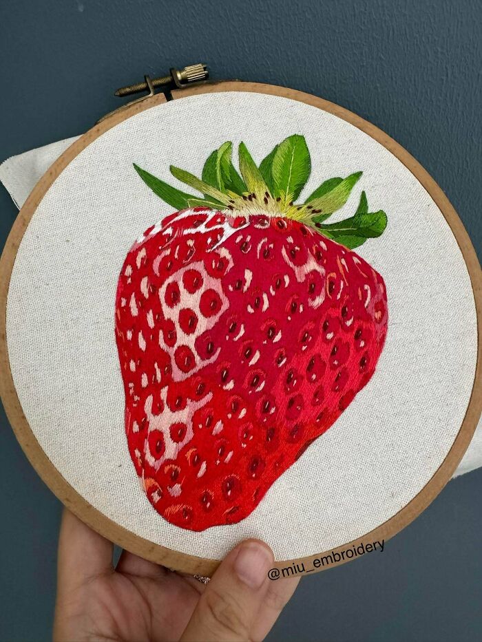 A detailed embroidery design of a large, ripe red strawberry stitched onto fabric inside a wooden hoop