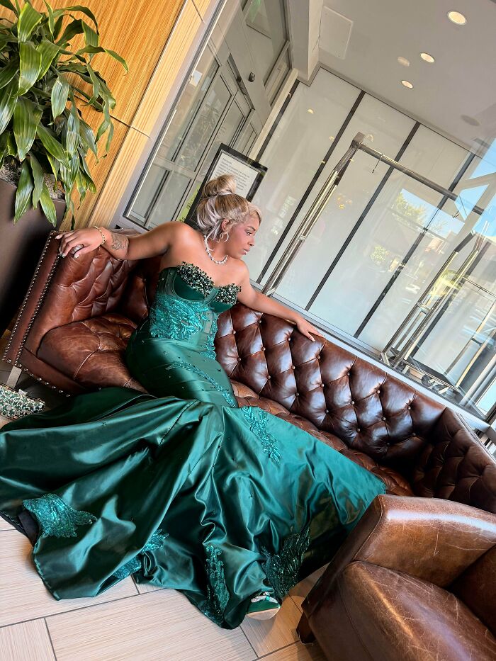 A woman in a beautiful green gown, a handmade project, sits elegantly on a leather sofa.