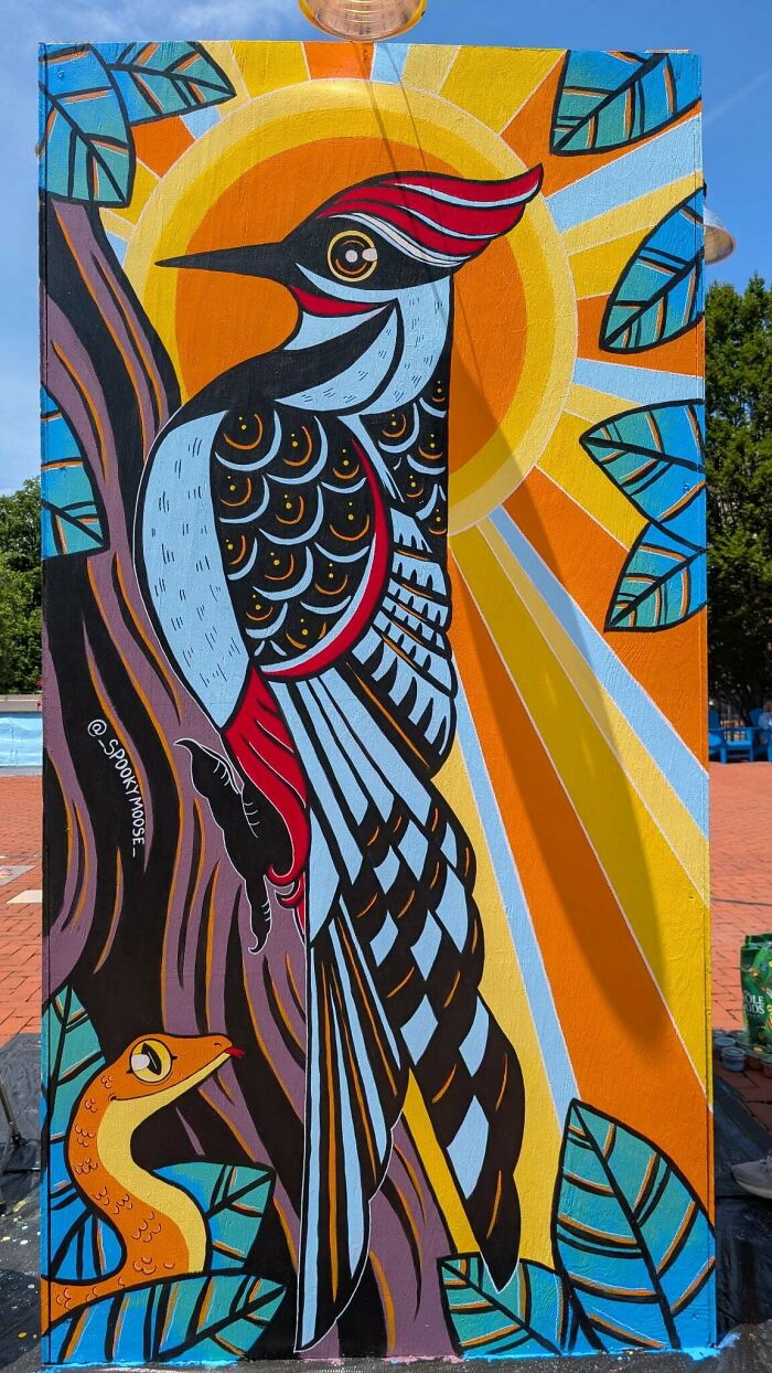A vibrant handmade mural depicting a woodpecker on a tree with a snake and a bright sun, a talented project.
