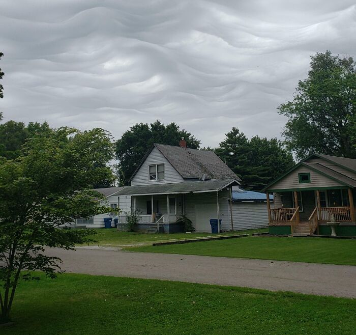 A neighborhood with houses under a sky filled with wavy, rippled clouds, a natural optical illusion.