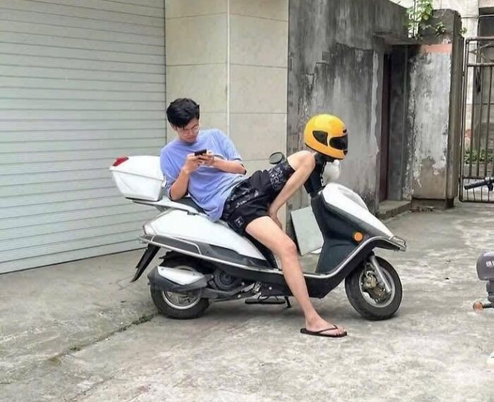 A man on a scooter, seemingly with another person whose body is an optical illusion of an elongated figure and a helmet head.