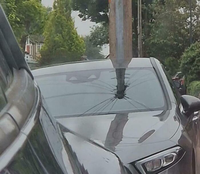 A car with a damaged windshield, struck by a pole, creating an unusual optical illusion.