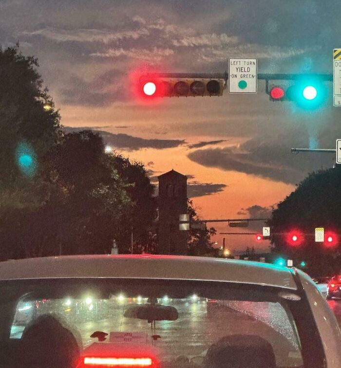 A cloudy sunset with traffic lights showing a red and green signal, creating an optical illusion.