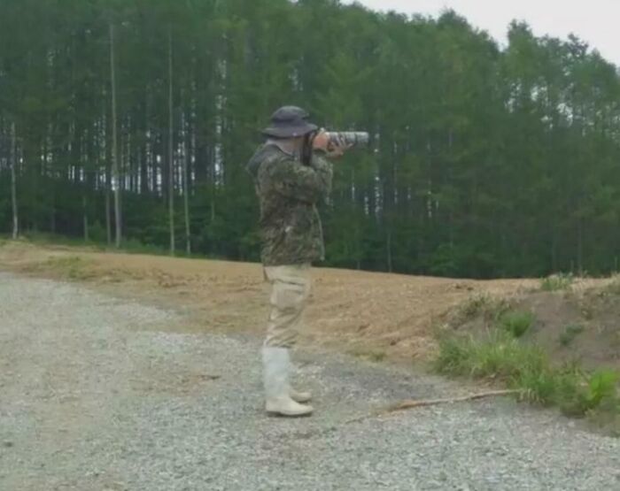 A man in camouflage taking a picture, blending into the trees to create an optical illusion.